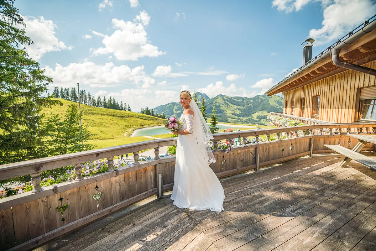 Eine Braut auf der Holzterrasse eines Chalets mit Bergblick
