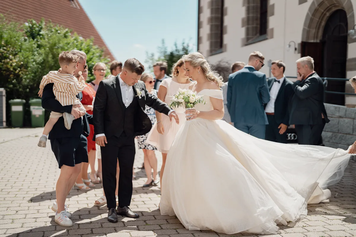 Ein Hochzeitspaar lacht mit seinen Gästen vor der Kirche